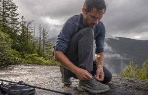 Why Hiking Shoe Technology Labels Tell You Almost Nothing Hiker retying a low-cut hiking shoe on wet granite, showing hiking shoe technology in real use