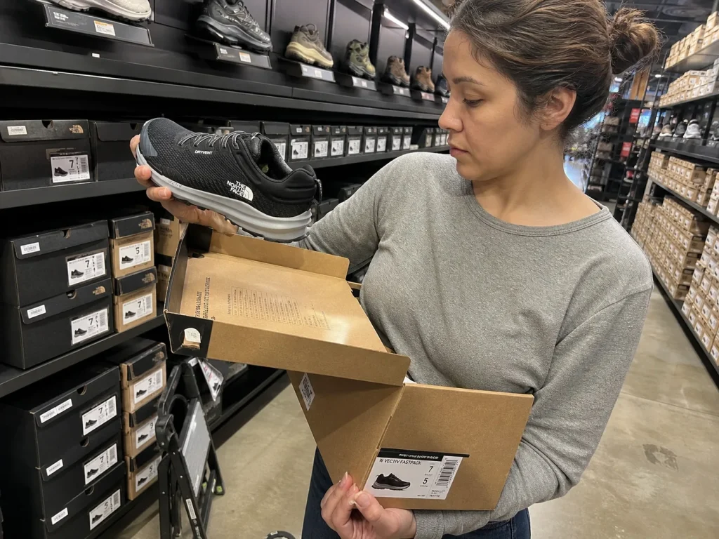 Shopper reading the spec label on a hiking shoe box in a store aisle