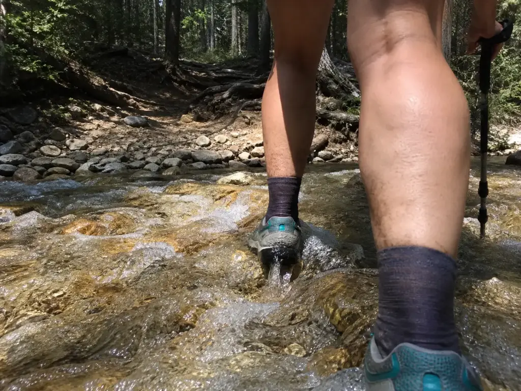 Hiker's feet in trail runners crossing a shallow stream, water draining through mesh
