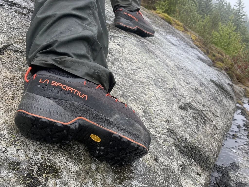 Sticky rubber outsole of an approach-style hiking shoe smeared onto wet granite slab
