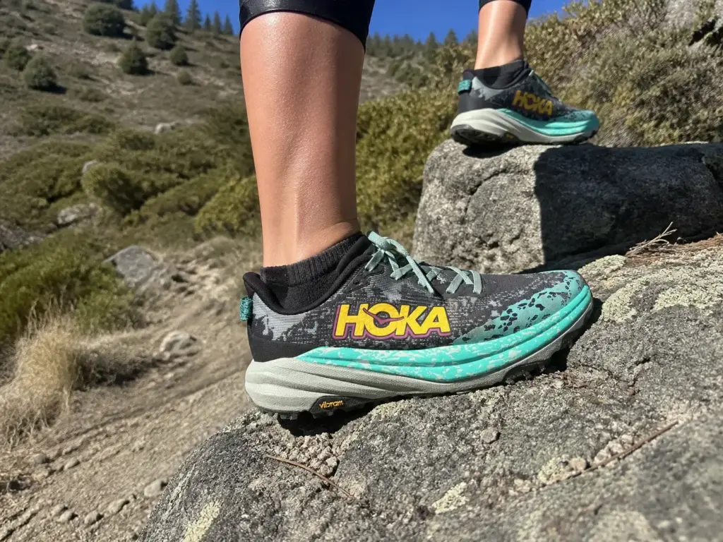 Close-up of a max cushion trail runner midsole on rocky trail showing stack height