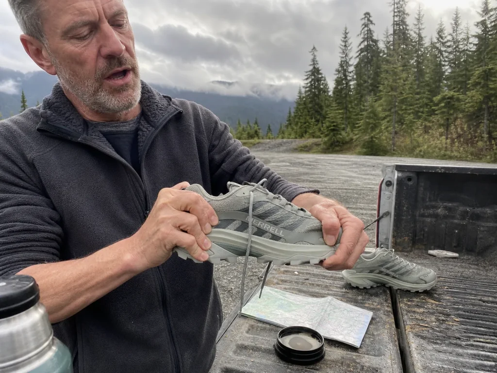 Hands twisting a low-cut hiking shoe to test torsional rigidity at a trailhead