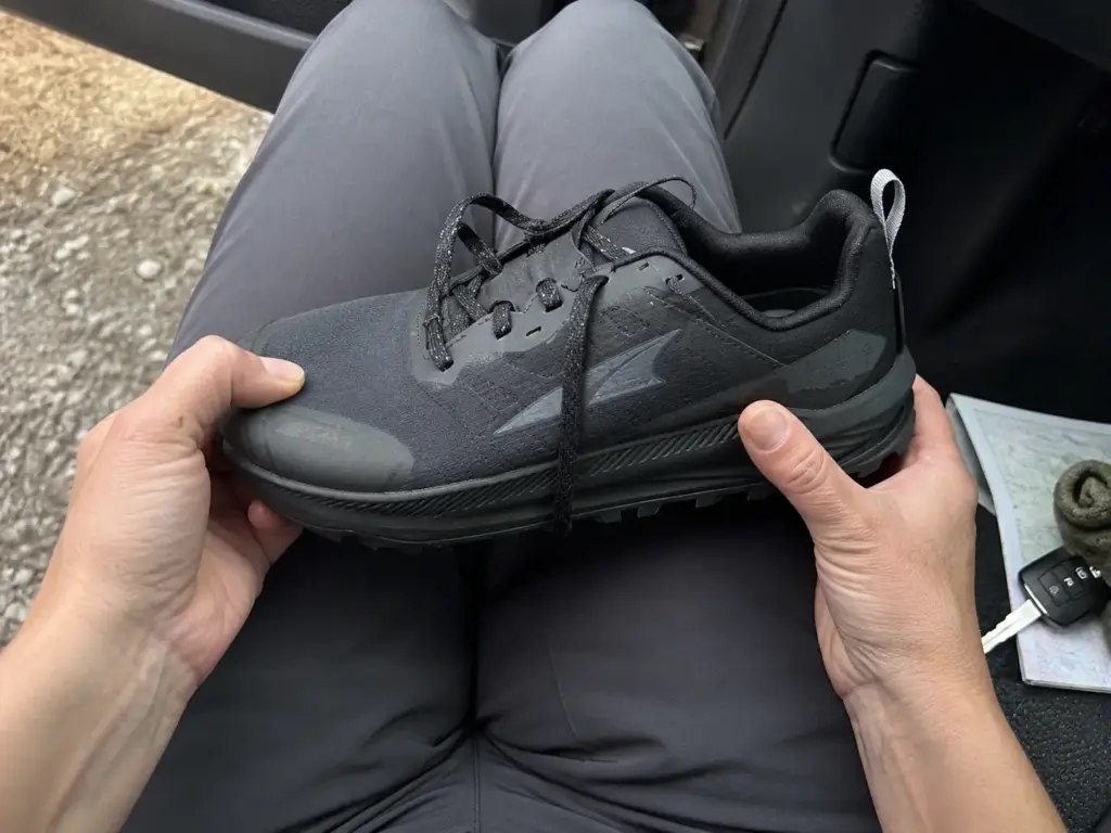Hands checking toe box room in a wide trail runner before a long hiking descent