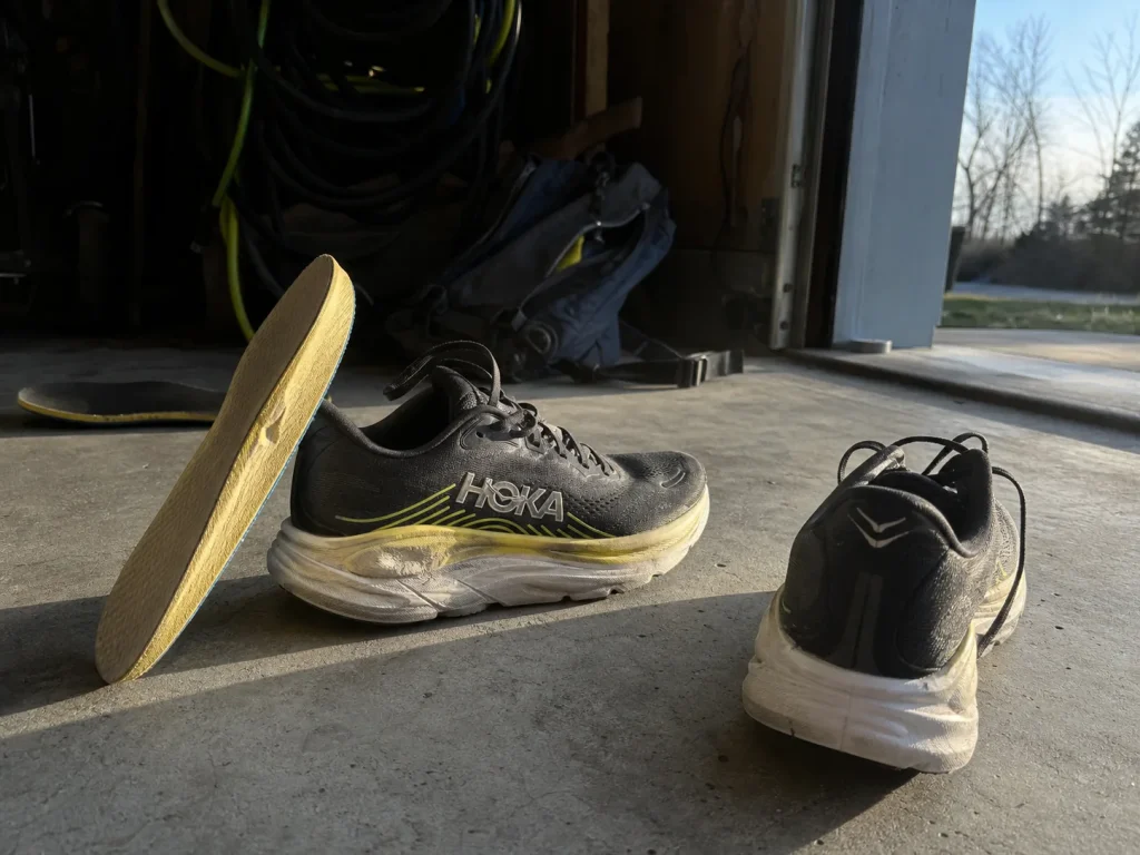 Two worn hiking shoes with insoles pulled out, comparing a packed-out midsole to good tread