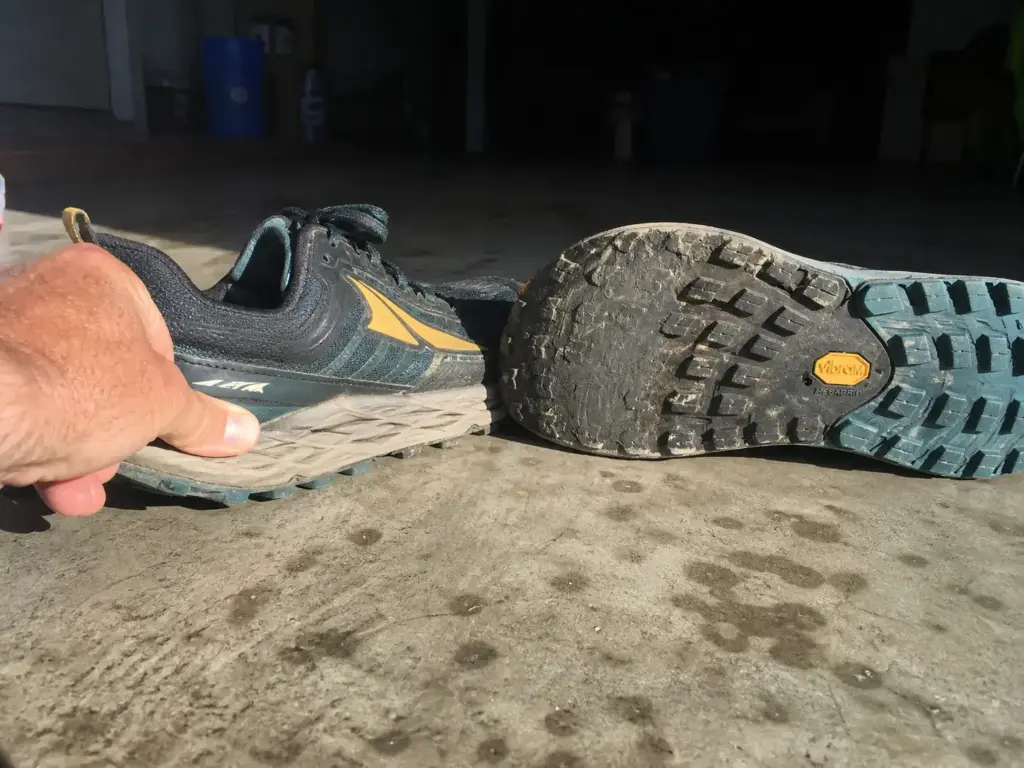 Two retired pairs of trail runners on a garage floor showing worn lugs and dead midsole
