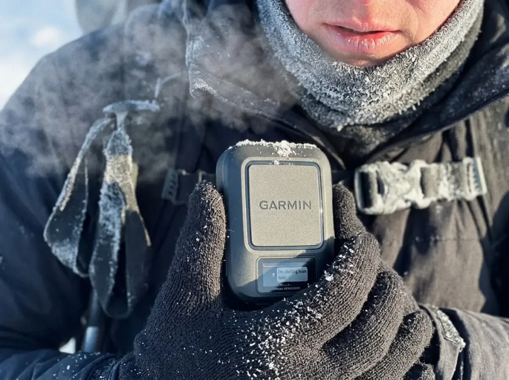 Gloved hiker checking a Garmin inReach Messenger in snow, testing cold-weather battery life