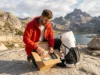 The 2026 Master Guide to Thru Hike Resupply Box Logistics A pristine thru-hiker sitting on a granite peak in the Sierra Nevada, organizing a resupply box filled with high-end hiking food, wearing a red Arc'teryx jacket and next to a white Hyperlite Mountain Gear pack, bathed in golden hour sunlight.