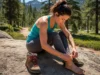 Treat Hiking Blisters: A Risk Assessment & Field Guide A fit female hiker in her late 20s sitting on a rock on a trail, treating a blister on her foot.
