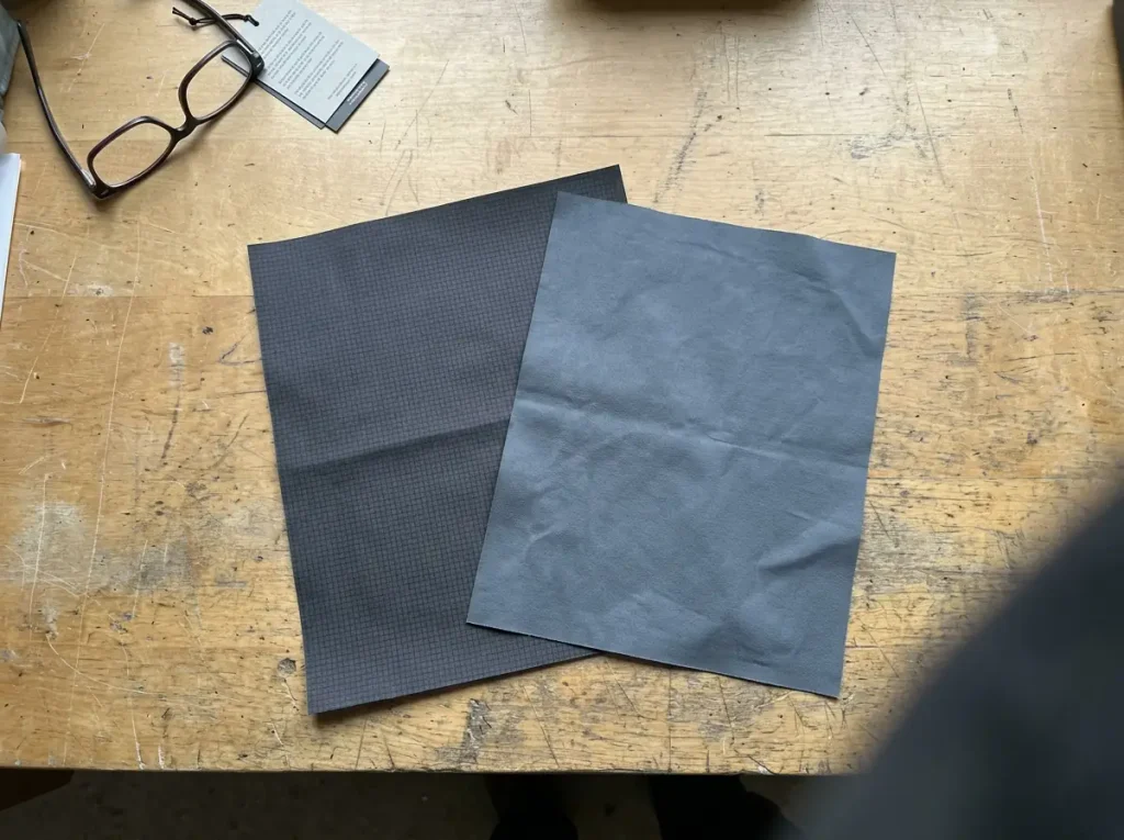 Two rain shell fabrics laid side by side on a workbench showing membrane construction differences