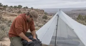 Silnylon vs Dyneema (DCF) What Fails First on Trail Hiker packing gear beside a pitched DCF shelter on a sandy desert bench, silnylon vs Dyneema choice in the field