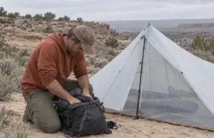 Silnylon vs Dyneema (DCF) What Fails First on Trail Hiker packing gear beside a pitched DCF shelter on a sandy desert bench, silnylon vs Dyneema choice in the field