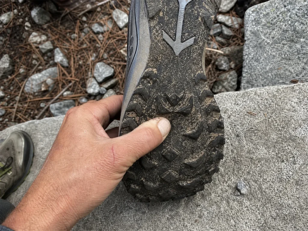 Saucony Peregrine 16 hiking shoe flipped sole-up on a rock, hand pressing the forefoot to feel the rock plate