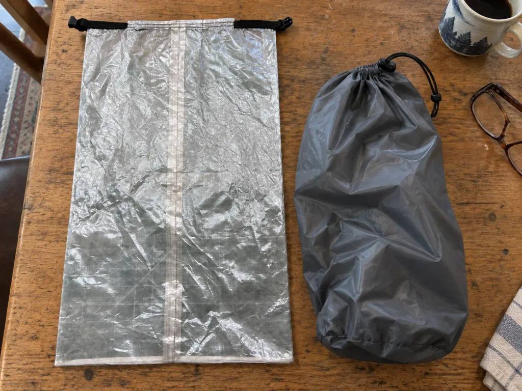 DCF roll-top bag beside a silnylon stuff sack on a table, showing how Dyneema and silnylon fabrics differ up close