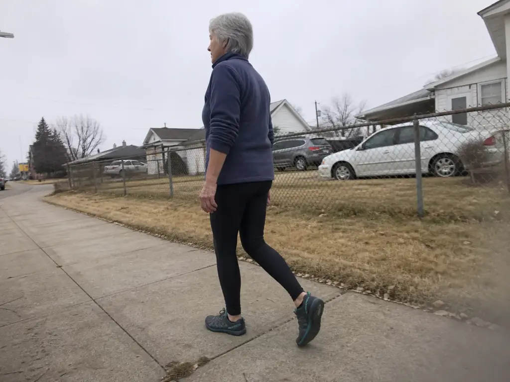 Hiker walking a suburban sidewalk in zero-drop shoes during the first month of transition