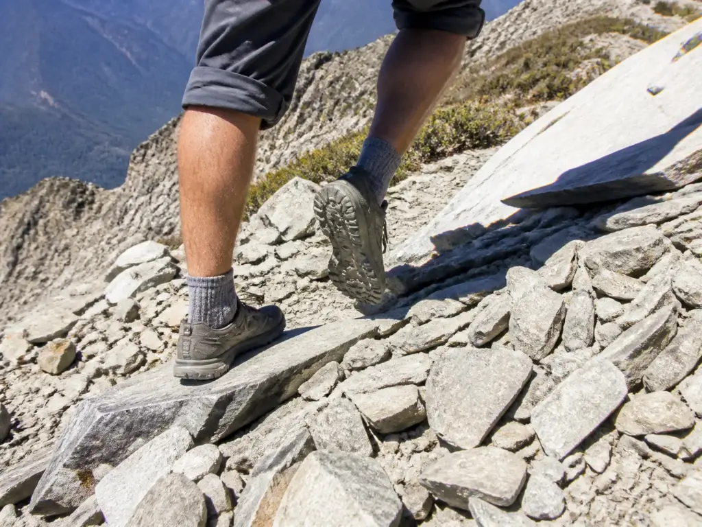 Close view of zero-drop hiking shoes stepping across sharp rock on an exposed ridge trail