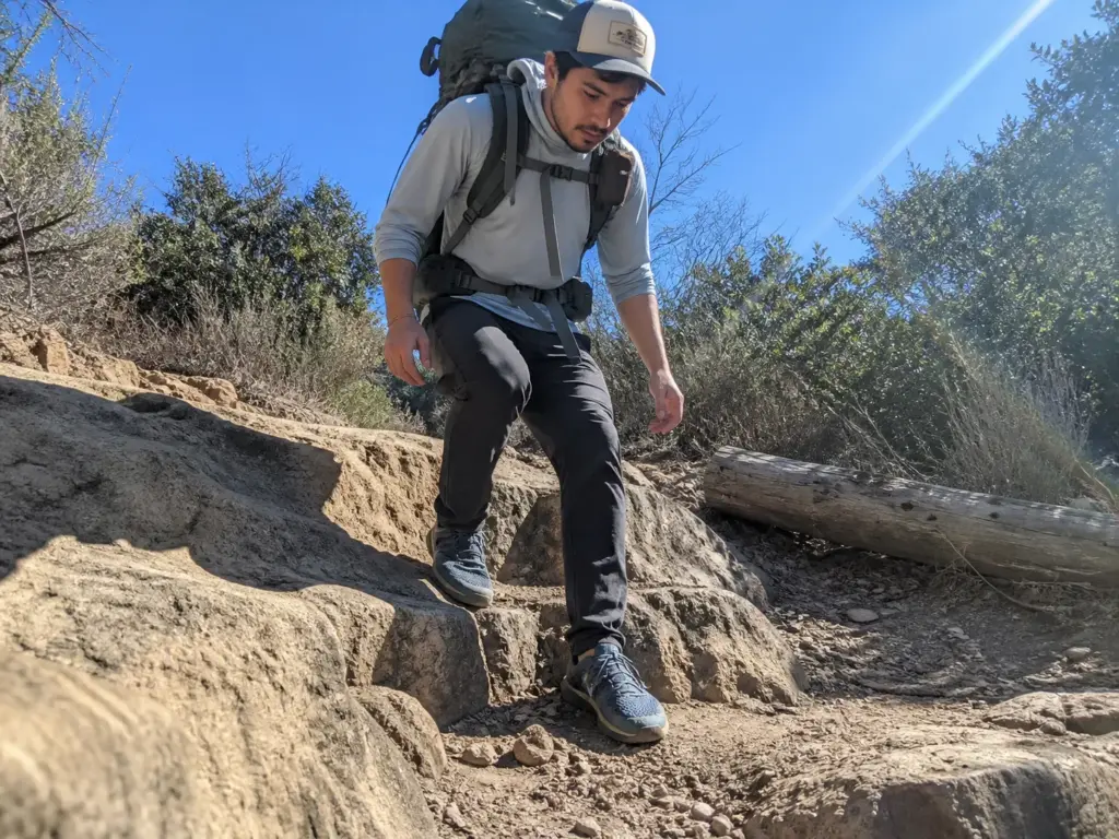 Backpacker descending a rocky step in zero-drop shoes while carrying a loaded overnight pack