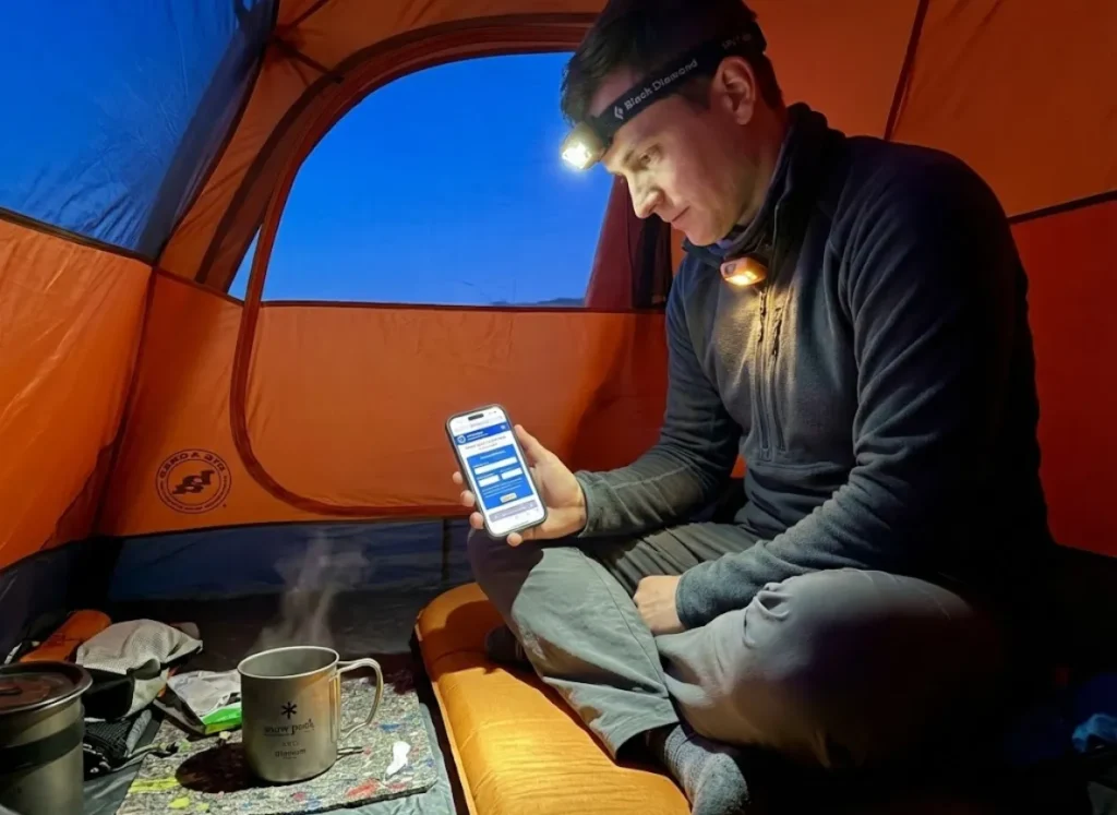 Hiker inside a Big Agnes tent using an iPhone to check NOAA magnetic declination data with a Black Diamond headlamp.