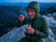 Cold Soaking Recipes Ranked by Calories & Clean-Up Hiker on a mountain ridge eating a cold soak meal from a Talenti jar using a Toaks titanium spoon while wearing a Patagonia jacket.