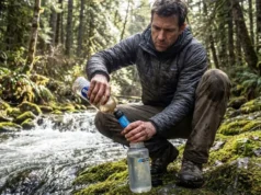 Giardia Symptoms: A Hiker’s Field Guide to Diagnosis A hiker in a Patagonia jacket filters stream water using a Sawyer Squeeze attached to a Smartwater bottle in a dense forest.