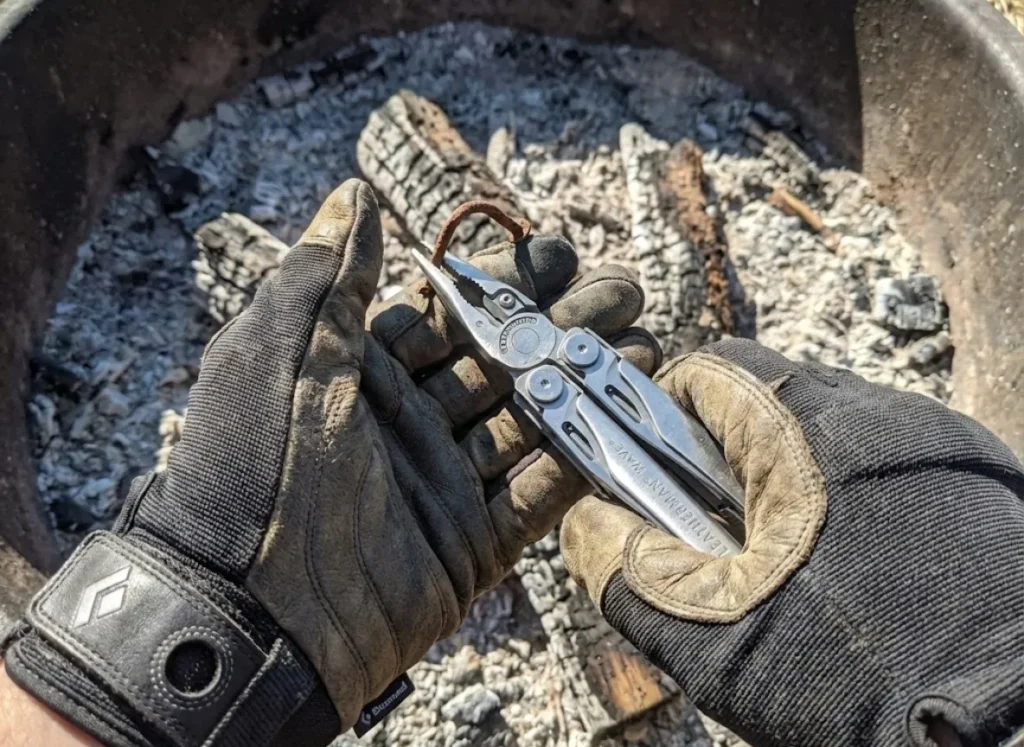 Hiker wearing Black Diamond gloves using a Leatherman tool to remove glass from a fire ring.