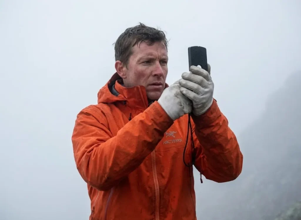 Mountaineer navigating through thick fog using a Suunto MC-2 compass and wearing an orange Arc'teryx jacket.