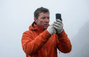Magnetic Declination Explained: Compass & GPS Guide Mountaineer navigating through thick fog using a Suunto MC-2 compass and wearing an orange Arc'teryx jacket.