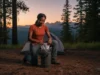 Mastering Backcountry Food Safety: The Complete System A confident female hiker carefully packing a bear canister at her backcountry campsite in a forest setting.