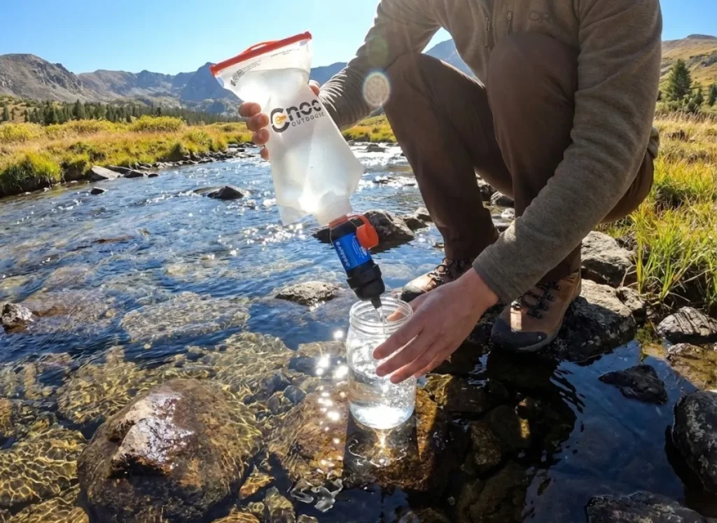 Hiker filtering water from a stream into a food jar using a Sawyer Squeeze and CNOC Vecto bag.