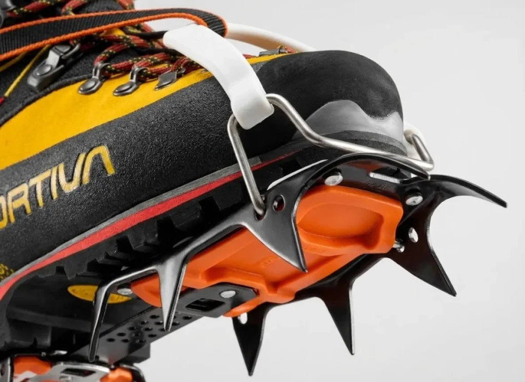 Macro studio shot of a La Sportiva Nepal Cube GTX mountaineering boot attached to a Petzl Vasak crampon, highlighting the rigid sole and steel spikes.