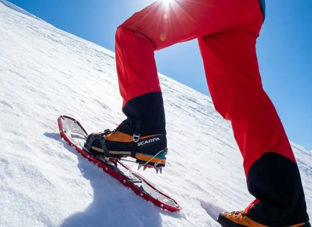 Low-angle view of a mountaineer's legs ascending steep snow on Mt. Shasta, wearing red Black Diamond pants and Scarpa boots, demonstrating the rest step.