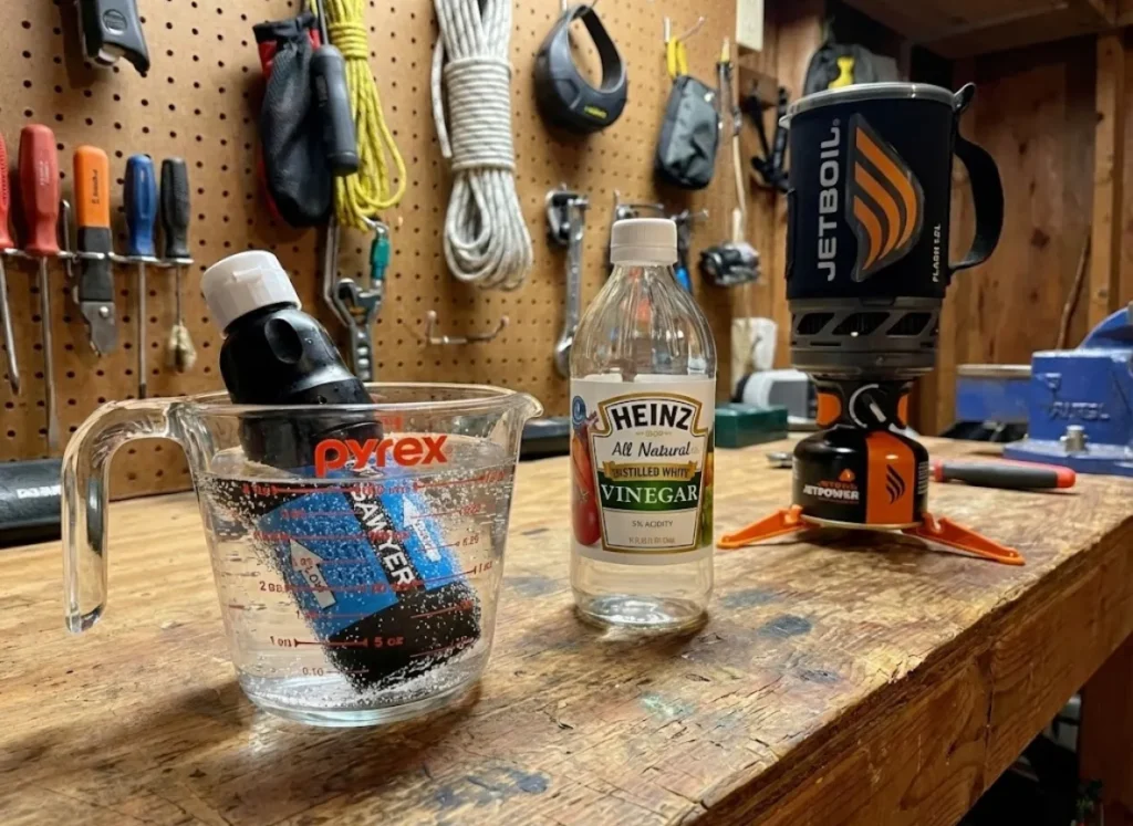 Sawyer Squeeze water filter soaking in a glass bowl of white vinegar to dissolve mineral deposits, next to a Jetboil stove.