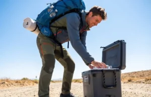 What Are Trail Angels? The Ultimate Etiquette & Safety Guide Thru-hiker with an Osprey backpack and Altra shoes grabbing a soda from a Coleman cooler at a trail crossing.