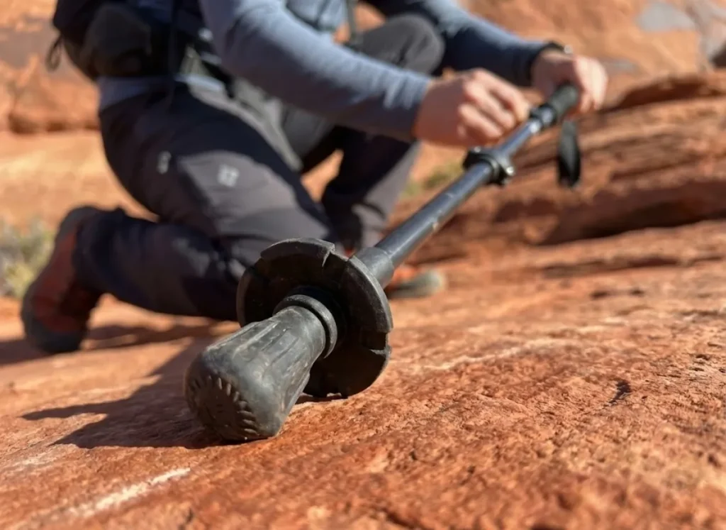 Close up of a rubber trekking pole tip gripping red sandstone rock to prevent scarring and erosion.