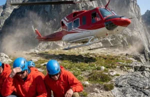 What Is Heli Hiking? Logistics, Gear & Skill Essentials Bell 212 helicopter taking off from a mountain ridge with hikers in Arc'teryx gear crouching in the foreground.