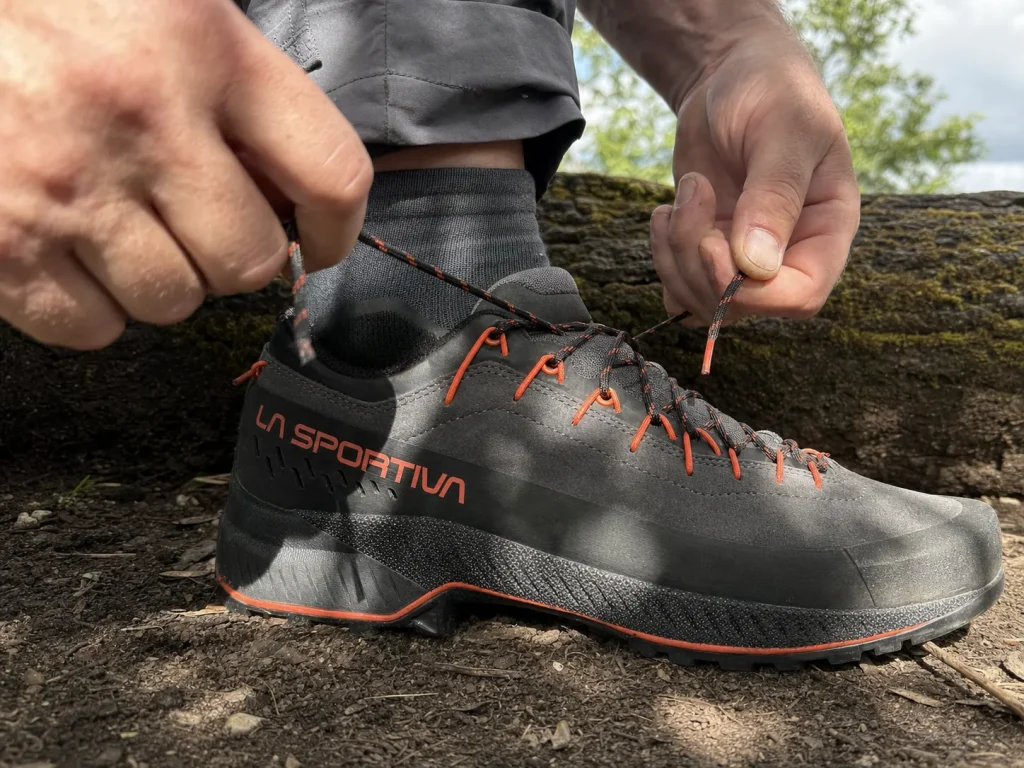 Hiker cinching approach shoe laces snug at a trailhead to check the precision fit