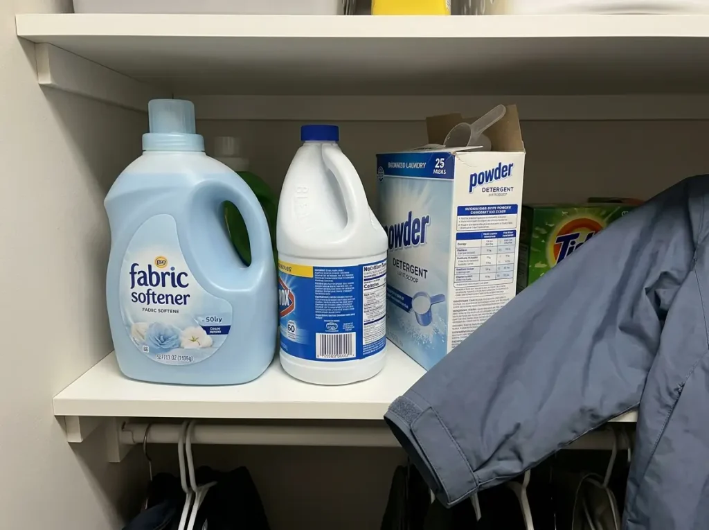 Fabric softener and bleach on a laundry shelf beside a rain jacket that should not meet them
