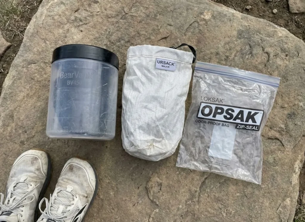 Comparison of a BearVault BV450, Ursack Major, and OPSAK bag next to Altra trail running shoes.
