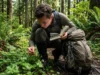 Edible Plants for Hiking: A Field Guide to Safe Nutrition A hiker crouched in a forest comparing a wild green plant to a photo in a field guide book.