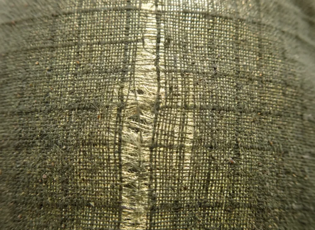 Extreme close-up macro shot of technical woven fabric backlit by the sun, showing warp and weft threads.
