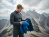 Fleece vs Down Jacket: A Hiker’s Layering System Guide A male hiker stands on a windy mountain trail, deciding between a fleece and a down jacket for his next layer.