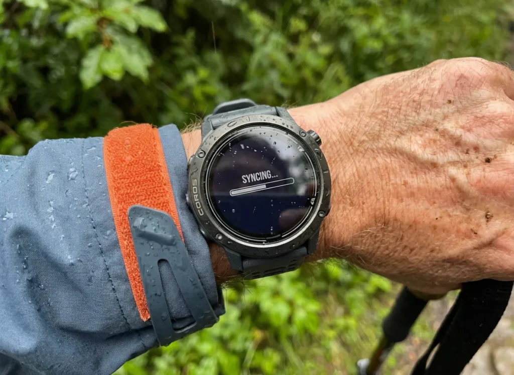 Close up of a rugged GPS watch on a wrist displaying a loading screen with water droplets on the glass.