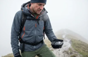 How to Create a GPX File: The Ultimate Hiker’s Guide A hiker in a yellow rain shell checks a handheld GPS device while standing in thick fog on a mountain ridge.