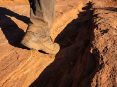 Hiking Ancient Trails: Historic Routes & Prep Close-up of dusty hiking boots stepping into a deep historical wagon rut carved into sandstone rock.