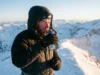 How to Keep Water From Freezing Hiking: The 3-Layer System A winter hiker on a snowy ridge drinking from a water bottle while shielding it from the wind.