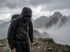 How to Wash Gore-Tex: The Ultimate Field-to-Laundry Guide A hiker walking through heavy rain on a mountain ridge, wearing a waterproof jacket that is saturated with water and no longer repelling rain.