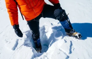 Post Holing Explained: Risks, Gear & Self-Rescue Close-up of a hiker's leg trapped deep in snow after breaking through the crust, illustrating the concept of postholing.
