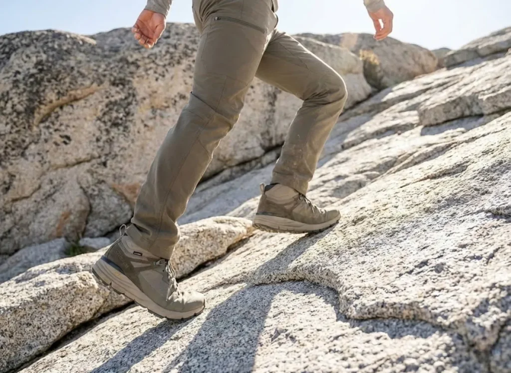 Close-up low angle view of a hiker's legs and boots scrambling up steep rocks with agility.