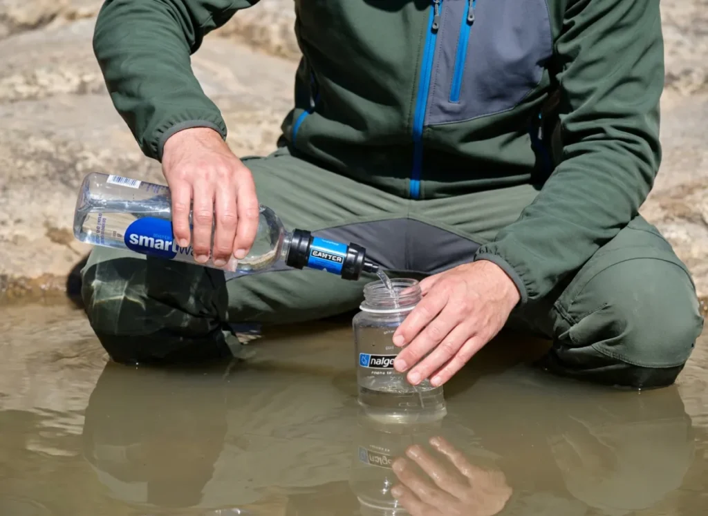 Hiker filtering water using a Sawyer Squeeze into a Nalgene bottle at a desert rock pool.