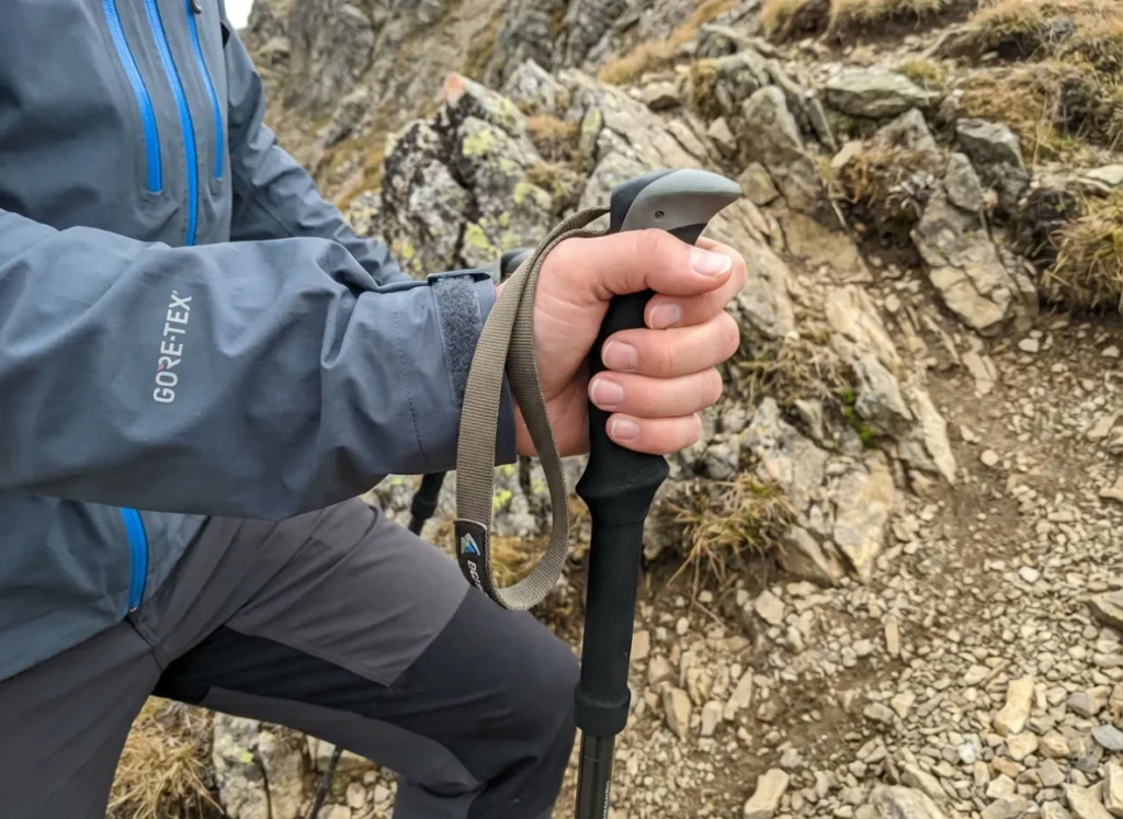 Hiker gripping trekking pole handle with the wrist strap unlooped for safety.