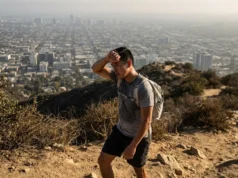 Best Urban Hiking Trails in the US: The Field Guide A hiker on a dirt ridge overlooking a smoggy city skyline, wiping sweat from their forehead.
